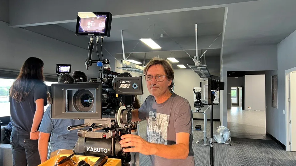 The owner of Geazoon beside a cinema camera mounted on a support in an indoor workspace.